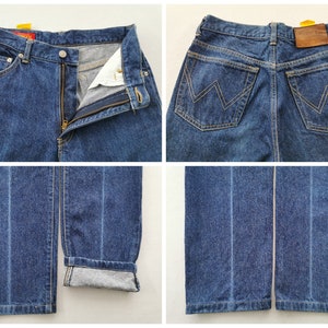 May include: A pair of blue denim jeans with a zipper fly and button closure. The jeans have a classic five-pocket design, a brown leather patch, and the brand name "Wrangler". The jeans are cuffed at the bottom, showing the interior fabric.