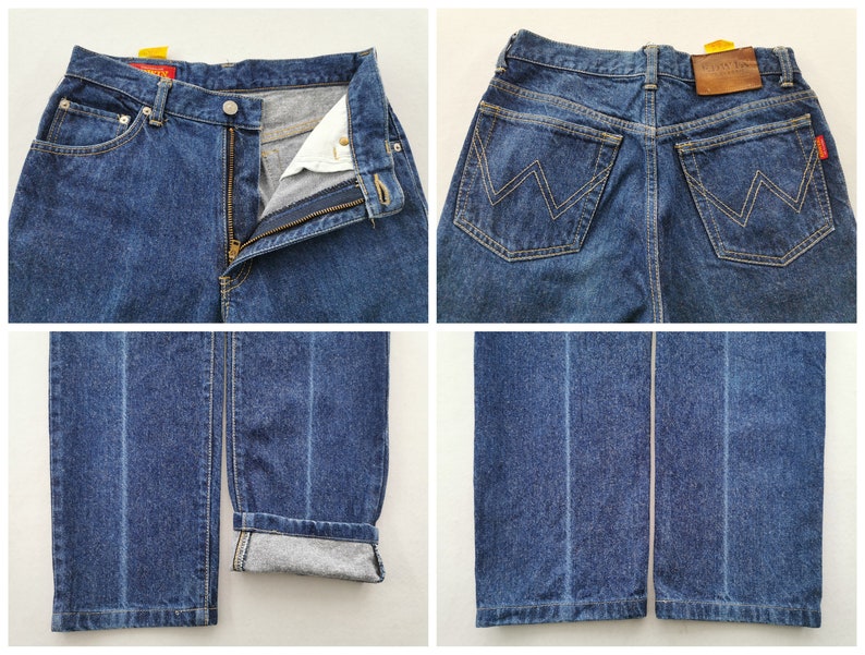 May include: A pair of blue denim jeans with a zipper fly and button closure. The jeans have a classic five-pocket design, a brown leather patch, and the brand name "Wrangler". The jeans are cuffed at the bottom, showing the interior fabric.