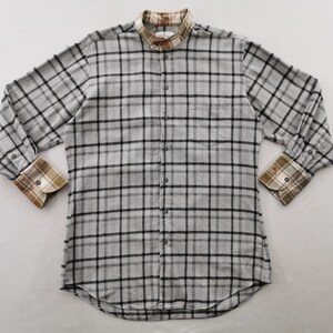 May include: A long-sleeved, button-down shirt in a gray and black plaid pattern. The shirt features a mandarin collar and contrasting plaid cuffs in shades of brown, tan, and white. A small logo is visible on the chest.