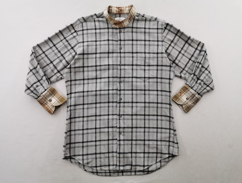 May include: A long-sleeved, button-down shirt in a gray and black plaid pattern. The shirt features a mandarin collar and contrasting plaid cuffs in shades of brown, tan, and white. A small logo is visible on the chest.