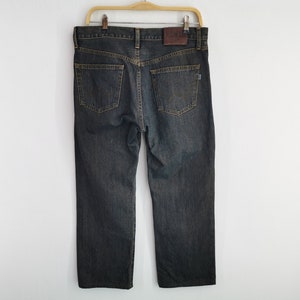 May include: Dark wash denim jeans hanging on a wooden hanger. The jeans have a classic five-pocket design, a straight leg, and a brown leather patch with the brand name on the back. The jeans are a medium weight.