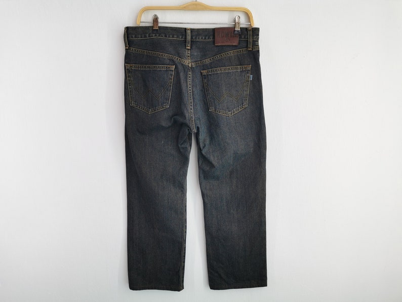 May include: Dark wash denim jeans hanging on a wooden hanger. The jeans have a classic five-pocket design, a straight leg, and a brown leather patch with the brand name on the back. The jeans are a medium weight.
