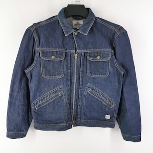May include: A dark blue denim jacket with a zip-up front, two chest pockets with button closures, and two side pockets. The jacket has a collar and is hanging on a black hanger against a white background.