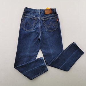 May include: Dark blue denim jeans with a classic five-pocket design. Features a leather patch and a red tag. The back pockets have a distinctive 'W' stitching. The jeans are laid flat, showcasing the straight leg cut.