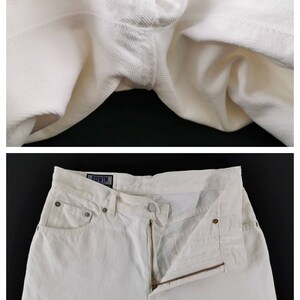 May include: Close-up and full shot of white denim jeans. The jeans have a zipper fly, pockets, and a button closure. The brand name "EDWIN" is visible on a tag. The fabric appears to be a sturdy, textured cotton.