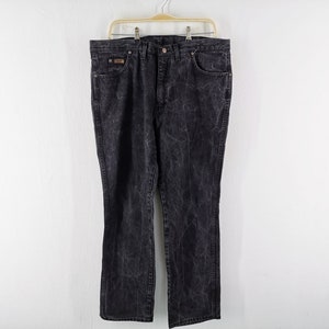 May include: Black denim jeans with a faded, textured appearance. The jeans have a classic five-pocket design, a button and zipper closure, and are hanging on a metal hanger against a white background. The jeans are a size 40.