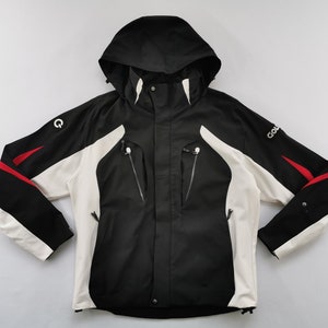 Pode incluir: Casaco com capuz preto, branco e vermelho com fecho de correr e v&aacute;rios bolsos. O casaco tem capuz e mangas pretas com pain&eacute;is brancos na frente e detalhes em vermelho. A palavra "GOL" &eacute; vis&iacute;vel na manga.