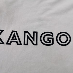 Peut inclure: Tissu blanc avec le mot "KANGOL" en noir, en gras et soulign&eacute;. Les lettres sont espac&eacute;es uniform&eacute;ment et centr&eacute;es, cr&eacute;ant un design &eacute;pur&eacute; et moderne. Le tissu semble lisse.