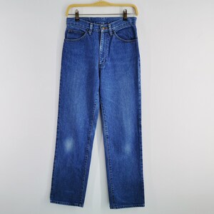 May include: Blue denim jeans hanging on a wooden hanger. The jeans have a classic five-pocket design, a button and zipper closure, and a straight leg. The jeans are a medium wash with some fading.