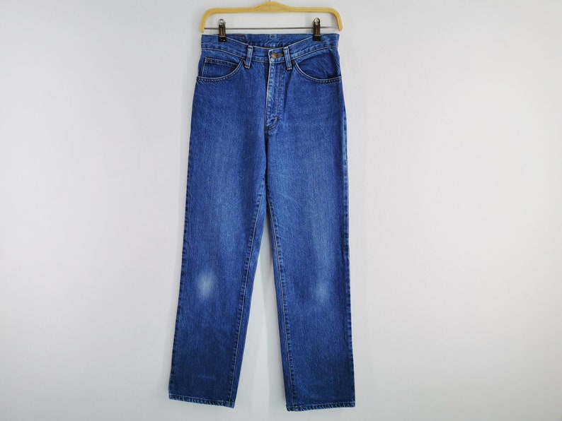 May include: Blue denim jeans hanging on a wooden hanger. The jeans have a classic five-pocket design, a button and zipper closure, and a straight leg. The jeans are a medium wash with some fading.