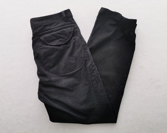 Puede incluir: Pantalones negros con cintura estructurada y trabillas para cinturón, un bolsillo grande con solapa redondeada en la parte superior del muslo y diseño de pierna cónica. La tela tiene un acabado mate con costuras visibles en bordes y bolsillos.