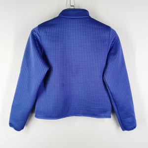May include: A blue zip-up jacket with a textured, grid-like pattern. The jacket has long sleeves and a stand-up collar. The garment is hanging against a white background.