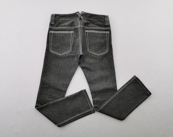 Puede incluir: Unos pantalones vaqueros de color gris oscuro con un sutil patrón de espiga y costuras blancas en contraste. La prenda incluye dos bolsillos traseros, trabillas para cinturón y un detalle en forma de V en la cintura.