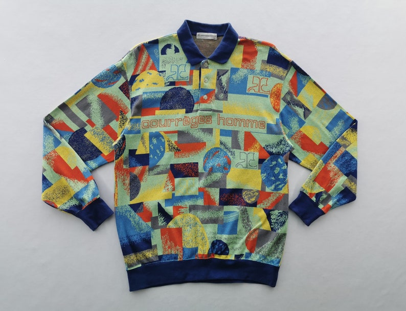 May include: A long-sleeved shirt with a colorful geometric pattern in shades of blue, yellow, red, and green. The shirt has a navy blue collar, cuffs, and hem. The text "COURR&Egrave;GES homme" is printed across the chest.