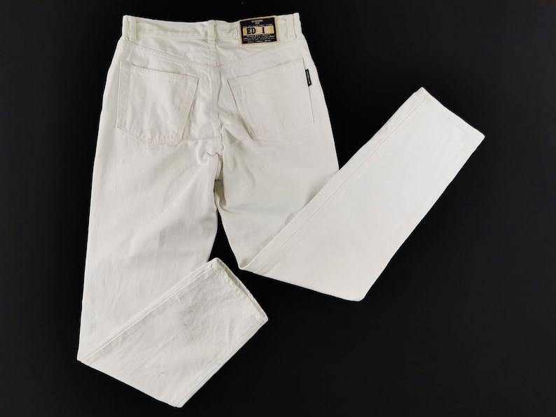 May include: Off-white denim jeans with a classic five-pocket design. The jeans have a straight leg cut and a small black label on the back pocket. The tag on the waistband reads "ED 1".