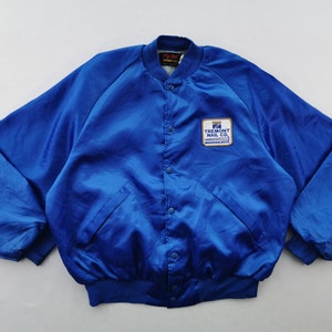 May include: A vibrant blue satin bomber jacket with a button-up front and two front pockets. The jacket features a patch on the chest with the text "TREMONT NAIL CO. WAREHAM, MASS."