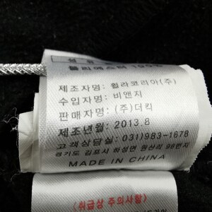 May include: A white tag with black text, attached to a black fabric. The tag includes text in Korean and English, with the words "MADE IN CHINA" at the bottom. The tag is attached with a silver string.