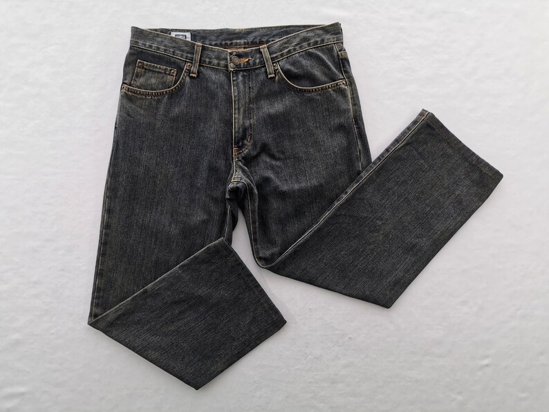 May include: Dark grey denim jeans with a classic five-pocket design. The jeans have a button and zip closure, belt loops, and a straight leg fit. The fabric appears pre-washed for a worn look.