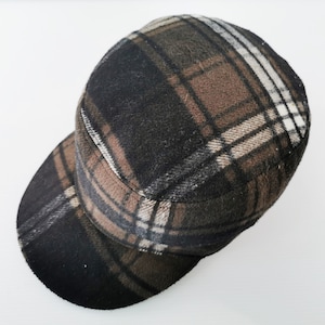 Può includere: Berretto a quadri con visiera piatta nei toni del marrone, nero e bianco. Il cappello ha una corona arrotondata e una visiera corta e rigida. Il tessuto ha un aspetto strutturato, forse lana. Uno stile classico per ogni occasione.