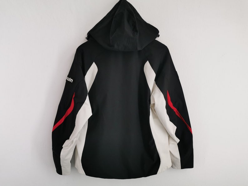Pode incluir: Casaco preto com capuz com detalhes em branco e vermelho. O casaco apresenta um corpo preto, pain&eacute;is laterais brancos e riscas vermelhas. A palavra "win" &eacute; vis&iacute;vel na manga esquerda. Vestu&aacute;rio exterior pr&aacute;tico.