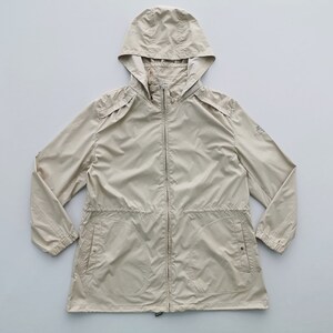 May include: A beige hooded windbreaker jacket featuring a full-length front zipper, long sleeves with elasticized cuffs, and two front pockets with snap button closures. The jacket includes a drawstring waist and shoulder epaulet details.