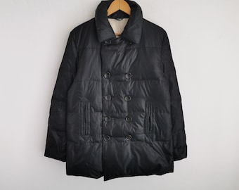 Puede incluir: Una chaqueta acolchada negra de doble botonadura con cuello ancho, costuras horizontales y seis botones oscuros dispuestos en dos filas verticales. La chaqueta incluye dos bolsillos verticales en la parte delantera y un forro interior claro.
