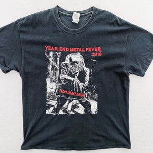 Könnte beinhalten: Schwarzes T-Shirt mit einer Grafik, die eine skelettartige Figur und den roten Text "YEAR END METAL FEVER 2016" zeigt. Das T-Shirt enthält auch den Text "TEAM HEAVY METAL".
