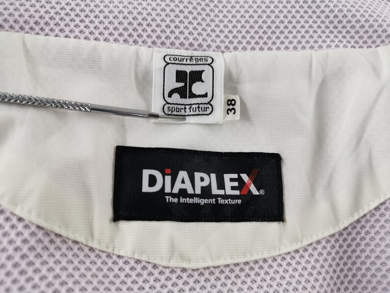 Puede incluir: Primer plano de una tela blanca y rosa claro con una etiqueta que dice "courr&egrave;ges sport futur" y "DiAPLEX The Intelligent Texture". La etiqueta tambi&eacute;n indica una talla 38.