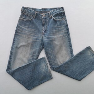 May include: Light blue denim jeans with a faded wash and a classic five-pocket design. The jeans have a button and zipper closure and are laid flat on a white surface. The jeans are a standard fit.