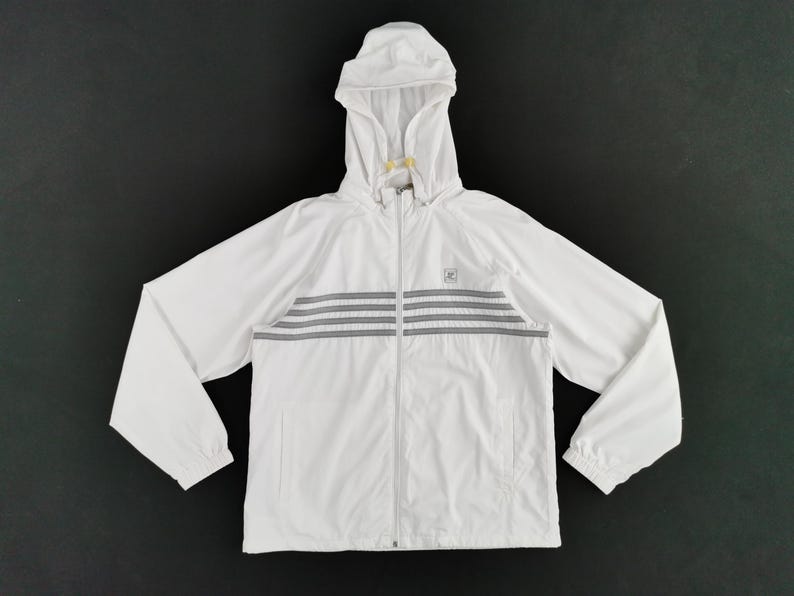 Puede incluir: Chaqueta blanca con capucha, cierre de cremallera y rayas horizontales grises en el pecho. La chaqueta tiene un peque&ntilde;o logotipo y una capucha con cord&oacute;n. Las mangas son largas y los pu&ntilde;os el&aacute;sticos.