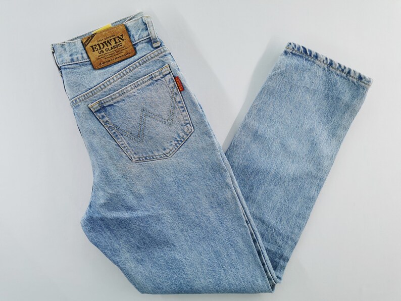 May include: Light blue denim jeans with a classic straight-leg fit. Features a back pocket with a stitched design and a leather patch with the brand name. The jeans have a faded wash and a vintage look.