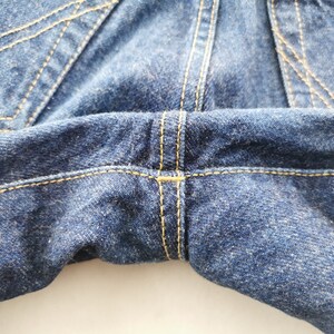 May include: Close-up of blue denim jeans, showcasing the stitching details. The image highlights the seams and the texture of the fabric. The stitching is in a contrasting yellow color, adding visual interest to the garment.