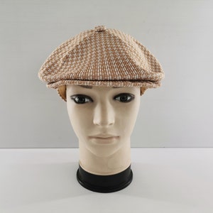 Puede incluir: Gorra de estilo newsboy con estampado marr&oacute;n y blanco. La gorra se muestra sobre una cabeza de maniqu&iacute;. Tiene una corona redondeada y una visera corta y r&iacute;gida. La tela tiene una apariencia texturizada.