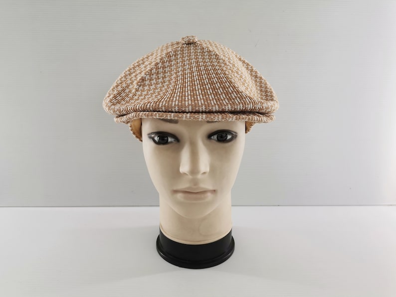 Puede incluir: Gorra de estilo newsboy con estampado marr&oacute;n y blanco. La gorra se muestra sobre una cabeza de maniqu&iacute;. Tiene una corona redondeada y una visera corta y r&iacute;gida. La tela tiene una apariencia texturizada.
