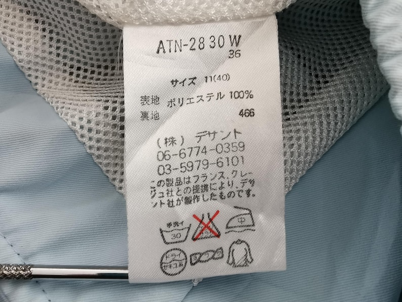 May include: A white clothing tag with Japanese text and care symbols. The tag includes the text "ATN-28 30 W" and "36". The tag also has washing instructions and the text "ポリエステル 100%" which translates to "Polyester 100%"