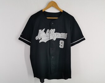 Puede incluir: Una camiseta de béisbol negra de manga corta con botones, que presenta la palabra Middlegrass en letras plateadas en el pecho. La camiseta incluye el número 9 en color plata debajo del texto y ribetes plateados en los puños.