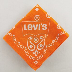 May include: Orange Levi's bandana with white paisley and floral designs. The Levi's logo is prominently displayed in white. The bandana is square-shaped and made of fabric.