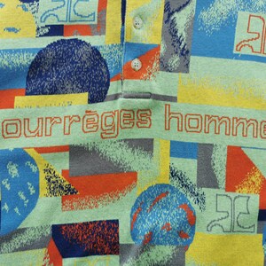 May include: A polo shirt with a colorful geometric pattern in shades of blue, yellow, orange, and gray. The shirt features the text "courr&egrave;ges homme" in orange. The shirt has a collared neckline and two white buttons.