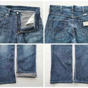 May include: Blue denim jeans with a button and zip fastening, front and back pockets, and the Wrangler logo. The jeans have a classic five-pocket design and a straight leg fit. The denim has a faded wash.