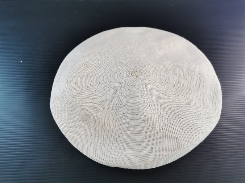 Puede incluir: Un sombrero boina beige con un dise&ntilde;o circular. El sombrero est&aacute; hecho de un material tejido y tiene una corona plana y redonda. La boina es un estilo cl&aacute;sico, adecuado para diversas ocasiones.