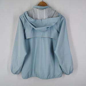 May include: A light blue hooded jacket with a full zipper and a white trim detail. The jacket is hanging on a wooden hanger against a white background. The jacket has a light grey lining inside the hood.