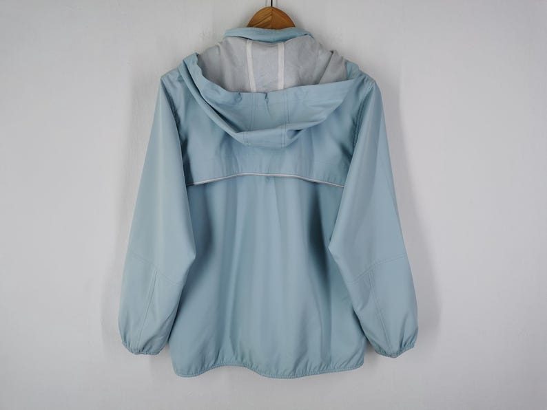 May include: A light blue hooded jacket with a full zipper and a white trim detail. The jacket is hanging on a wooden hanger against a white background. The jacket has a light grey lining inside the hood.