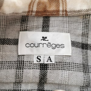 May include: Close-up of a plaid shirt with a label that reads "courr&egrave;ges" in black text. The shirt has a gray, white, and brown plaid pattern. The label also has the size "S A" printed on it.