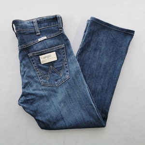 May include: Blue denim Wrangler jeans with a classic five-pocket design. The jeans have a straight leg, a button and zip closure, and the Wrangler logo on the back pocket and waistband. The jeans are neatly folded.