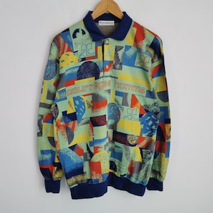 May include: A long-sleeved shirt with a colorful geometric pattern in shades of blue, yellow, red, and gray. The shirt features a navy blue collar and cuffs, and the text "courreges homme" is printed across the chest.