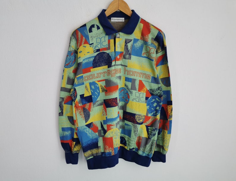 May include: A long-sleeved shirt with a colorful geometric pattern in shades of blue, yellow, red, and gray. The shirt features a navy blue collar and cuffs, and the text "courreges homme" is printed across the chest.