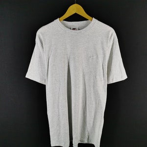 May include: A heather gray t-shirt with short sleeves, hanging on a wooden hanger. The shirt features a small Nike logo on the upper left chest. The background is a dark gray.