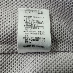Puede incluir: Una etiqueta blanca con texto e iconos japoneses, adherida a una tela gris claro texturizada. La etiqueta incluye instrucciones de lavado y el texto "MADE IN CHINA".