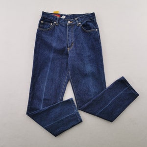May include: Dark blue denim jeans with a classic five-pocket design. The jeans have a straight leg cut and a button and zipper closure. The stitching is a contrasting yellow color. The jeans are laid flat on a light gray surface.