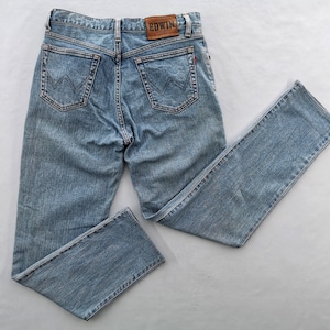 Può includere: Jeans in denim blu chiaro con un classico design a cinque tasche. Presenta una toppa in pelle con il marchio "EDWIN" sul retro. I jeans hanno un taglio dritto e un lavaggio sbiadito.